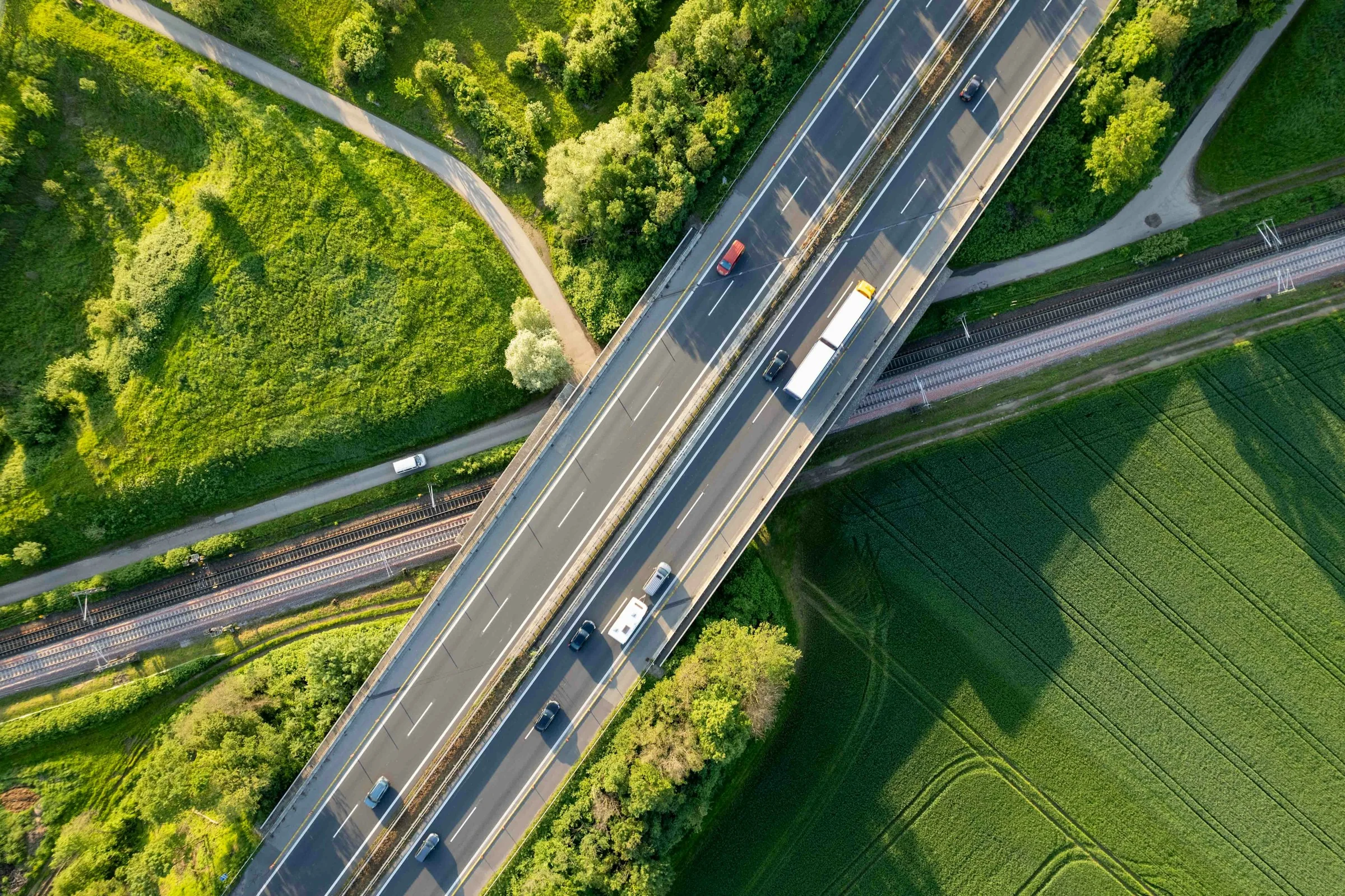 Vista aérea de uma rodovia entre áreas verdes, com caminhões em trânsito